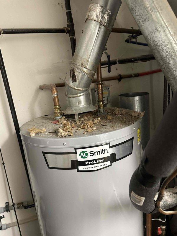 Completed installation of new ductwork in renovation area, including proper insulation of silver ducts running between exposed ceiling joists. System connects to existing A.O. Smith ProLine Commercial Grade water heater with appropriate ventilation piping secured with metal tape at joints.