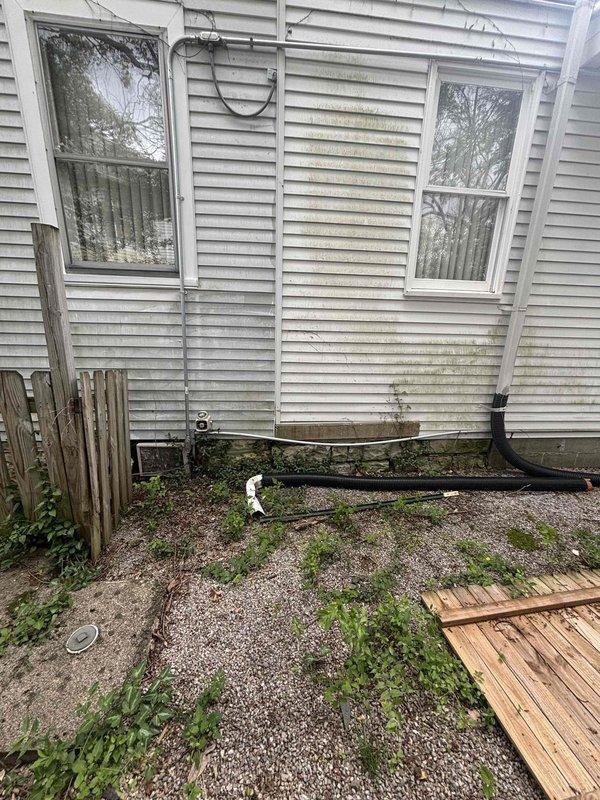 Conducted follow-up site inspection to document incomplete work items from previous HVAC installation. Photographed exterior condenser location showing drainage concerns and vegetation growth around foundation, as well as interior attic laundry area where ductwork and ventilation components require completion. Documented current conditions for scheduling final installation phases.