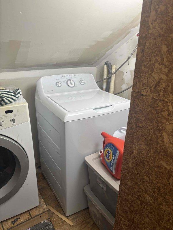 Conducted follow-up site inspection to document incomplete work items from previous HVAC installation. Photographed exterior condenser location showing drainage concerns and vegetation growth around foundation, as well as interior attic laundry area where ductwork and ventilation components require completion. Documented current conditions for scheduling final installation phases.