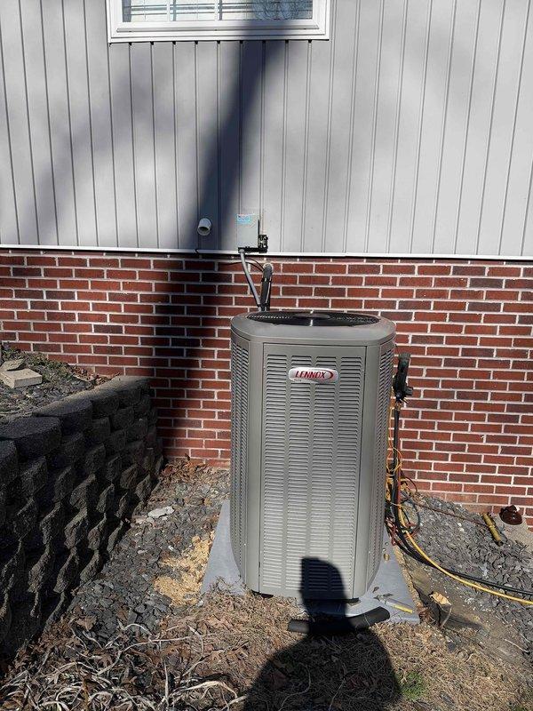 Installed new Lennox EL16XCV-036-230B04 complete HVAC system with outdoor condenser unit mounted on concrete pad adjacent to brick exterior wall. System includes proper refrigerant line connections, electrical wiring, and drainage setup with PVC drain pipe. Unit was tested and verified to be functioning according to manufacturer specifications.