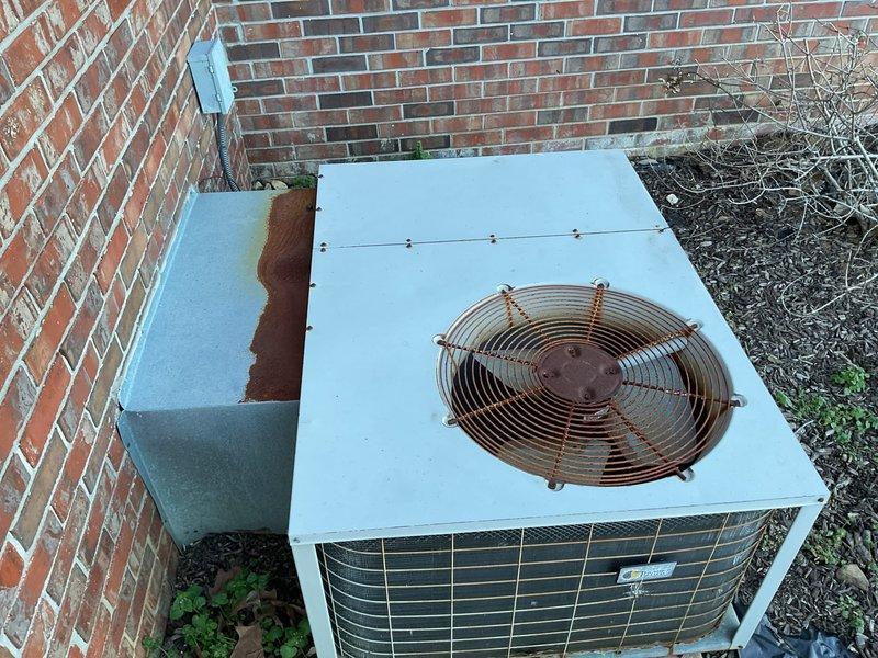 Conducted comprehensive evaluation of aging outdoor HVAC system showing significant deterioration including extensive rust on fan assembly, weathered housing, and corrosion on adjacent components. Unit positioned against brick exterior wall exhibits end-of-life indicators and requires full system replacement as discussed with customer who is interested in the tankless water heater promotion with complete system installation.