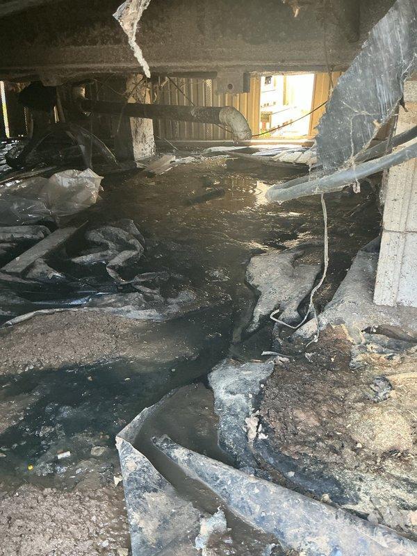 Responded to emergency call for water discharge at rear of mobile home. Upon inspection, located source approximately 4-5 feet beneath structure in crawlspace. Main drain line had separated at elbow connection where pipe transitions to ground level, causing active water flow into crawlspace area. Extensive moisture saturation and standing water observed throughout confined area beneath mobile home. Documented existing conditions with photographs showing compromised drainage system, waterlogged surfaces, and deteriorated crawlspace environment. Advised property owner of findings and provided assessment of repair requirements for disconnected drain line connection.