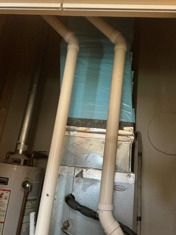 Completed follow-up visit to perform leak search on HVAC system in utility closet. Inspected air handler unit, associated refrigerant lines, and PVC condensate drainage system for potential leak sources. Documented equipment configuration including air handler positioning relative to water heater and thermostat wiring at wall-mounted control location for service records.